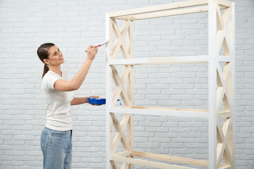 žena maľuje vysokú drevenú policu na bielo