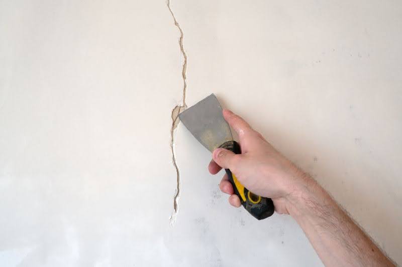 muž so špachtľou opravuje prasklinu v stene