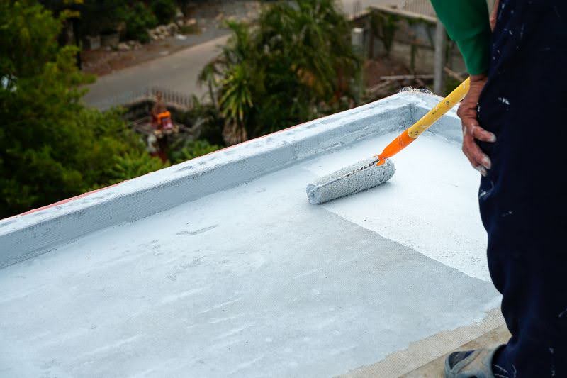 muž natiera plochú strechu izolačným náterom