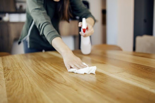 žena čistí drevený stôl handričkou a čistiacim prostriedkom