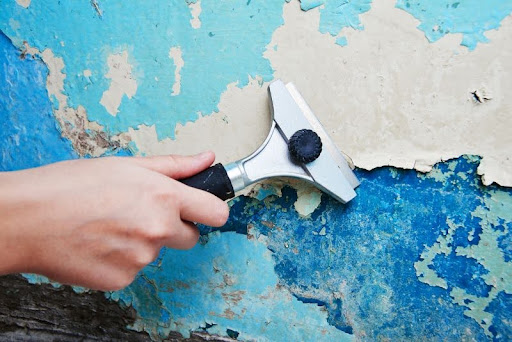 odstraňovanie starej modrej farby zo steny pomocou škrabky